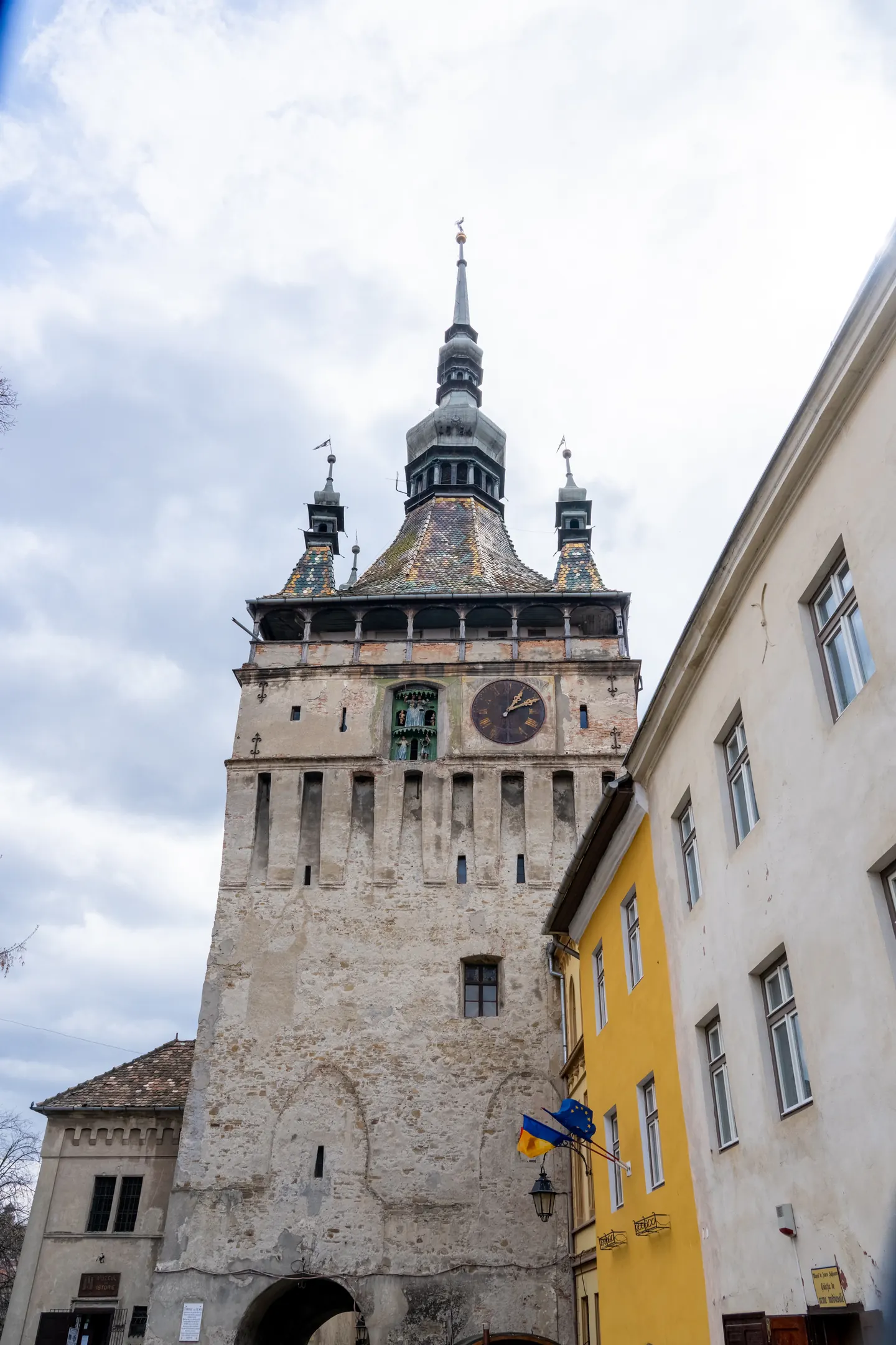A close view of Sighișoara’s Clock Tower, colorful roof tiles and neighboring yellow façade